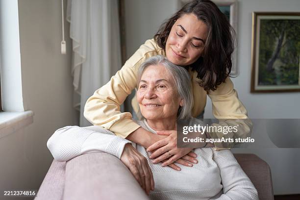 daughter hugging senior mother from behind holding hands - assistente social imagens e fotografias de stock