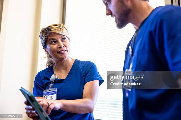 des infirmières discutent des résultats d’examen d’un patient dans un couloir près de la fenêtre - blouse dexamen médical photos et images de collection