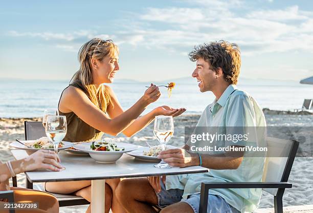 couple sharing food at beach restaurant enjoying romantic dinner - table for two stock pictures, royalty-free photos & images