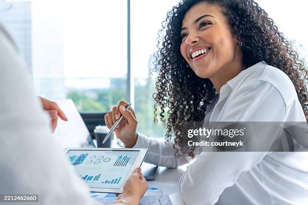 two business women meeting in the office. one woman is holding a digital tablet showing financial data - bank manager stock pictures, royalty-free photos & images