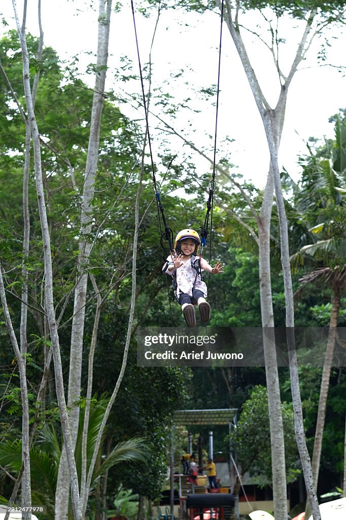 Happy Young Girl Riding Flying Fox Amidst Lush Trees