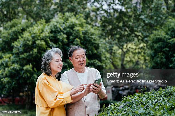asian senior couple using smart phone in public park. - old man smart stock pictures, royalty-free photos & images