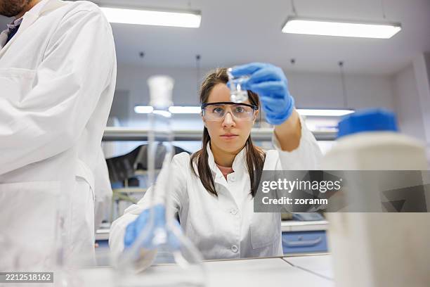 estudiante femenina en clase de práctica con colegas en el laboratorio, con bata de laboratorio, gafas protectoras y guantes - laboratorio de ciencia fotografías e imágenes de stock