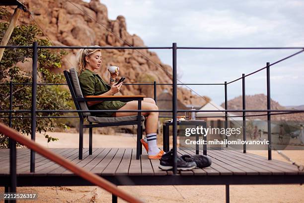 safari enthusiast using her cellphone and drinking coffee at safari lodge - kenyan culture stock pictures, royalty-free photos & images