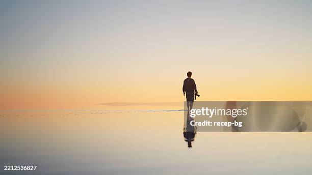 mann alleinreisender, der seine kamera hält und während des sonnenuntergangs auf der flachen wasseroberfläche läuft - küstenlandschaft stock-fotos und bilder