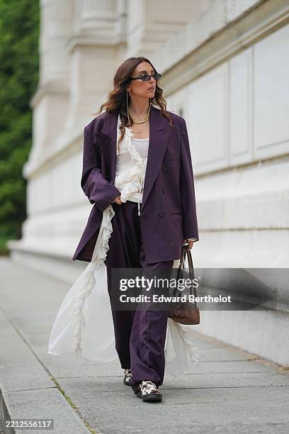 Gabriella Berdugo wears an oversized burgundy vintage suit by Courreges featuring a double-breasted blazer and relaxed-fit trousers, layered over a...