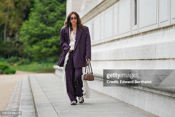 Gabriella Berdugo wears an oversized burgundy vintage suit by Courreges featuring a double-breasted blazer and relaxed-fit trousers, layered over a...