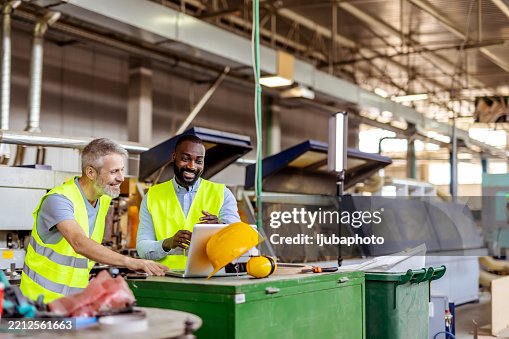 Two Workers Collaborating in a Production Facility While Reviewing Plans Two Workers Collaborating in a Production Facility While Reviewing Plans