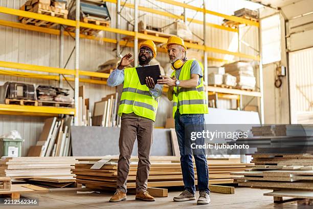 two engineers discussing work plans in a busy warehouse environment - construction material stock pictures, royalty-free photos & images