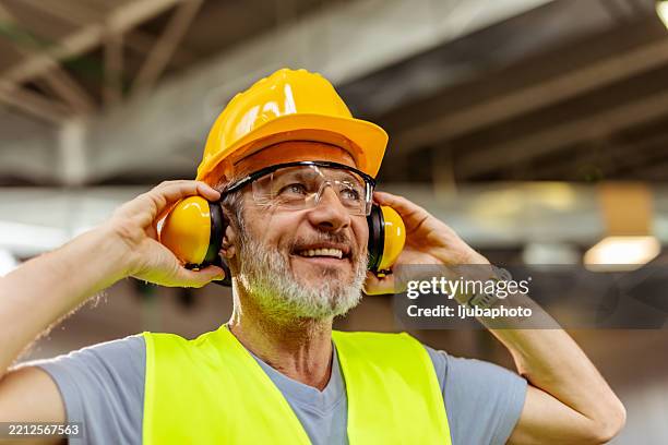 trabajador de la construcción de alto nivel con equipo de seguridad sonriendo en un área industrial - equipo de seguridad fotografías e imágenes de stock