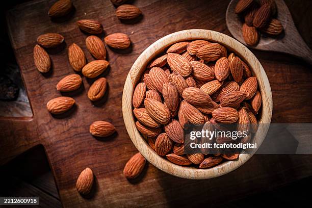 overhead view of fresh organic peeled almonds in a bowl shot on rustic table - almond stock pictures, royalty-free photos & images