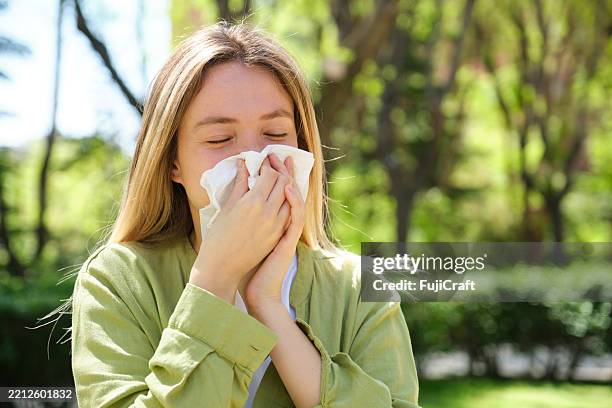 giovane donna che starnutisce in un parco durante la stagione delle allergie primaverili - allergia foto e immagini stock