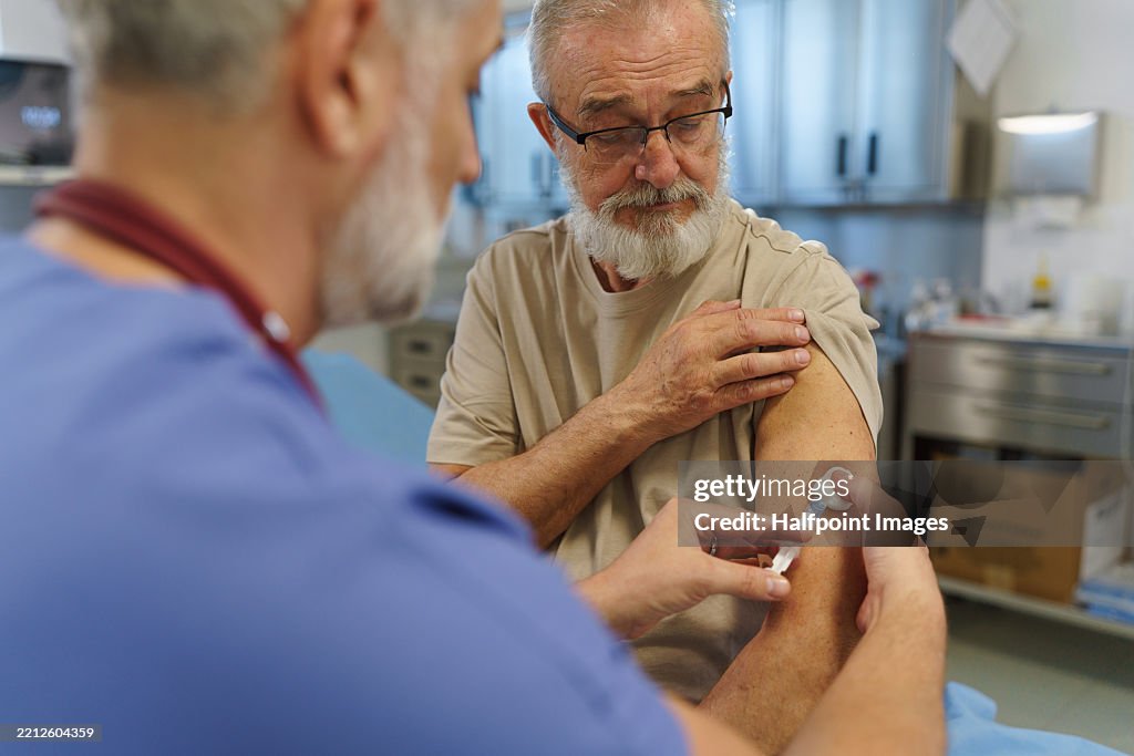 Doctor administering vaccine to older patient during preventive check-up.