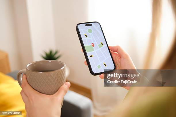 frau, die eine mitfahrgelegenheits-app auf ihrem handy verwendet, während sie zu hause kaffee trinkt - gps stock-fotos und bilder