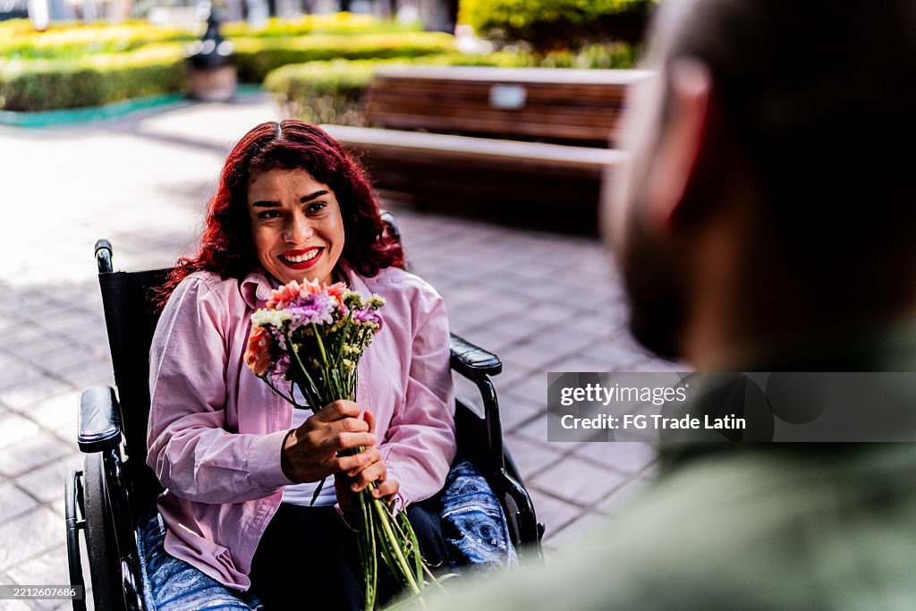 Young wheelchair woman receiving flowers and talking to boyfriend outdoors