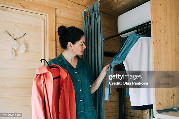 woman choosing clothes from closet in wooden tiny house - chambre bien rangée photos et images de collection