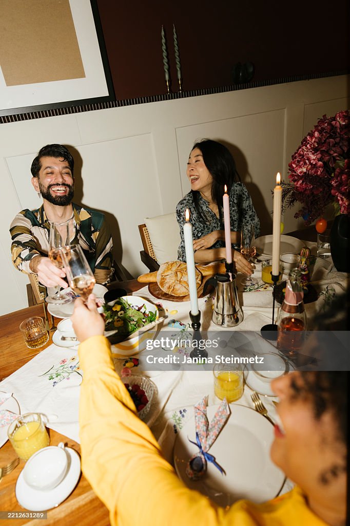 View from above of three friends laughing and toasting with champagne at dinner