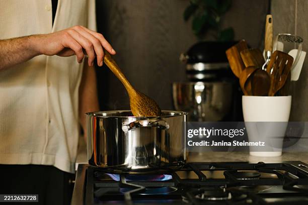 a hand stirs a wooden spoon in the cooking pot - cooking pan stock pictures, royalty-free photos & images