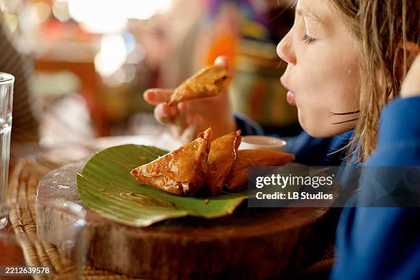 child enjoying freshly cooked samosas on a banana leaf in a cozy dining setting. tanzania, africa - samosa stock pictures, royalty-free photos & images