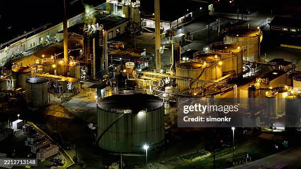 illuminated industrial facility at night with golden lighting and complex structures in pittsburgh - oil explorations pensylvania imagens e fotografias de stock