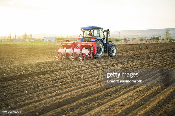 vista trasera del agricultor plantando semillas con tractor y sembradora en el campo rural al atardecer - sembrar fotografías e imágenes de stock