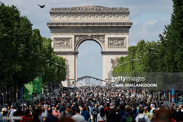 Pedestrians walk along the Champs-Elysees avenue as the Arc de Triomphe dominates the skyline, during a "car free" day in Paris on May 4, 2025. One...