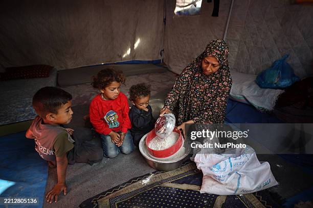 Displaced Palestinian woman sieves expired flour to remove mold and insects to make bread for her children in their displacement tent at the Yarmuk...