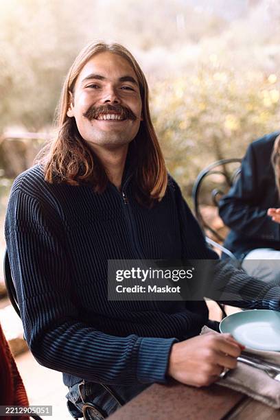 portrait of smiling young man sitting at dining table during dinner party - facial hair stock pictures, royalty-free photos & images