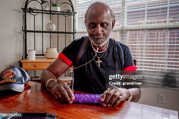 elderly african-american man in his seventies with oxygen tube sorting prescriptions at the kitchen table in his home - medical oxygen equipment stock pictures, royalty-free photos & images