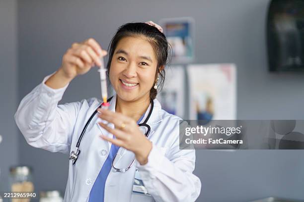 doctor preparing syringe with medication in a clinical environment - medizinische fakultät stock-fotos und bilder