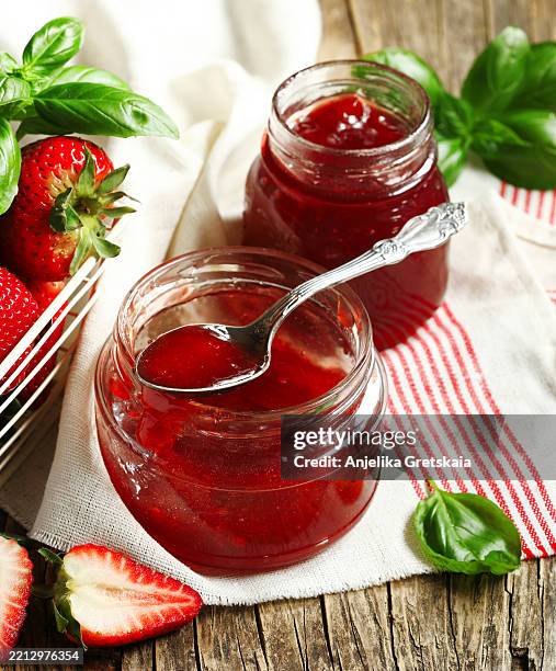 homemade delicious strawberry jam with basil in a glass jar and fresh strawberries on table - marmellata foto e immagini stock