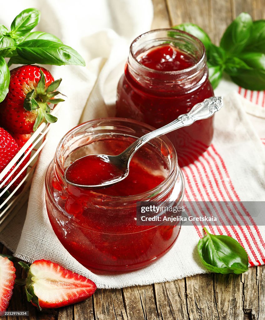 Homemade delicious strawberry jam with basil in a glass jar and fresh strawberries on table