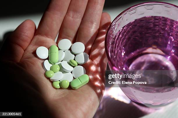 female's hand grabbing heap of small pills against blurred pink drinking glass background - antibiotikaresistent stock-fotos und bilder