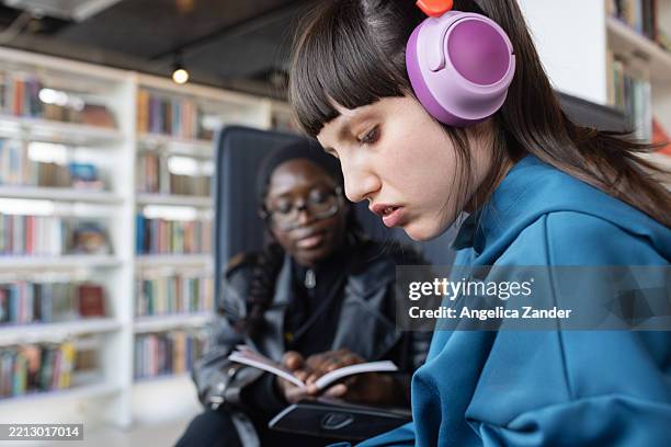 behindertenbetreuer beim lesen mit neurodivergentem teenager in der bibliothek - autismus stock-fotos und bilder