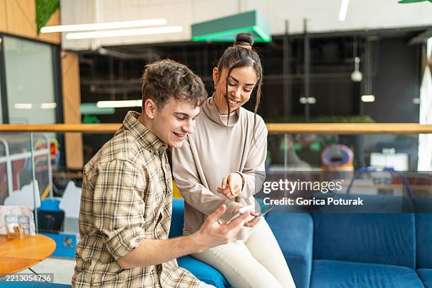 young colleagues sharing a laugh while using a smartphone in office breakroom - 18 20 2025 stock pictures, royalty-free photos & images