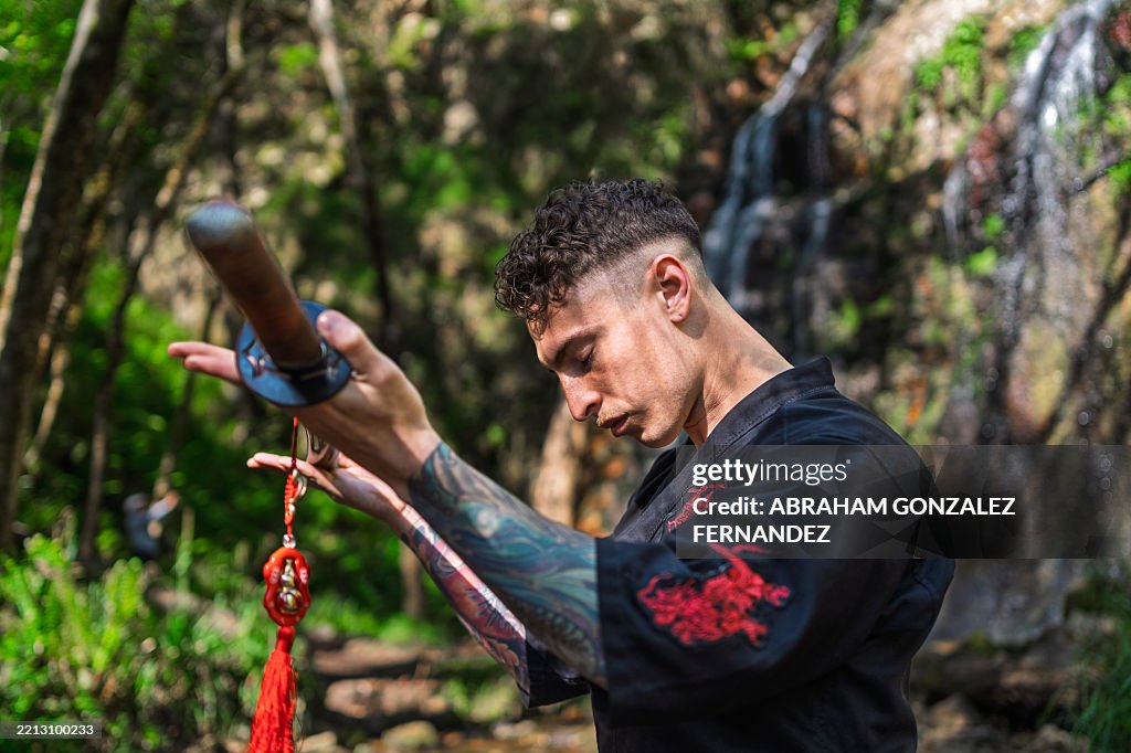 Junger Mann, der Iaido praktiziert, ein Katana hält, während er in der Nähe eines ruhigen Wasserfalls in einem ruhigen Wald meditiert, und Achtsamkeit und Konzentration verkörpert