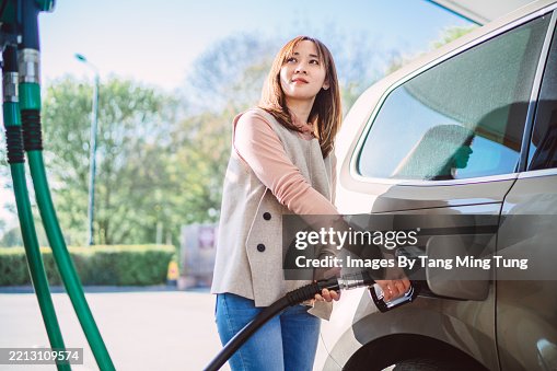 Woman refueling her car at a gas station on a sunny day Woman refueling her car at a gas station on a sunny day
