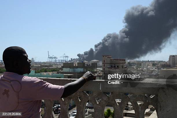 Man watches as smoke billows after a drone strike on the port of Port Sudan on May 6, 2025. Drones struck the airport and targeted an army base in...