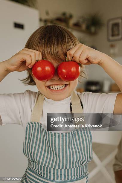 smiling child holding tomatoes as goggles in a kitchen setting - homegrown produce stock pictures, royalty-free photos & images