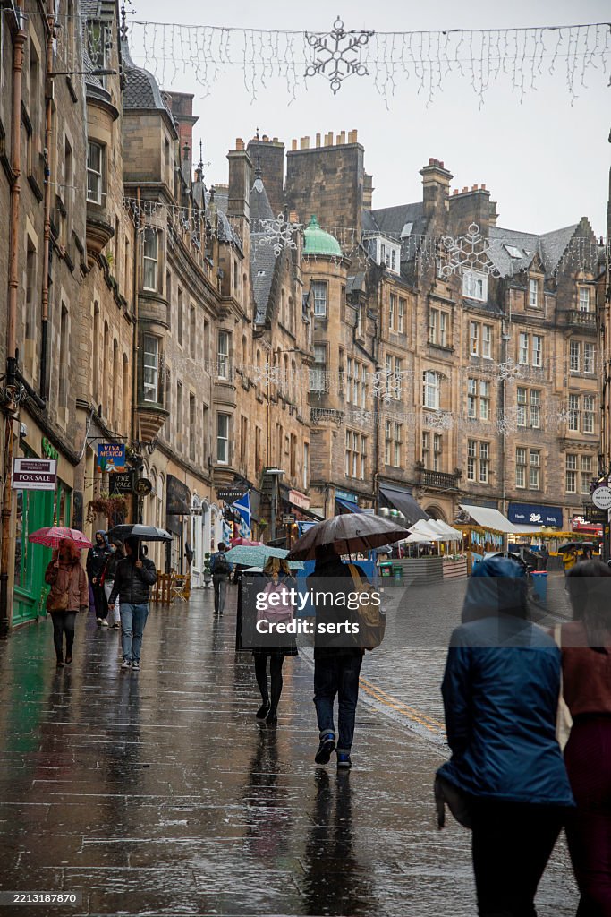 People Walking with Umbrellas on a Rainy Autumn Day Along Cockburn Street in Edinburgh Old Town on a Christmas Day in Scotland, UK