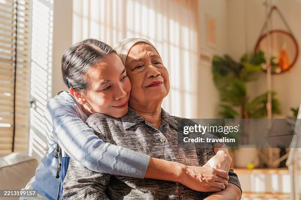 asian family, old woman hugging her daughter and cancer with sad people on a sofa in the home living room during recovery. love, trust or comfort with a sick senior female parent embracing daughter and sick mother hugging - perdão imagens e fotografias de stock