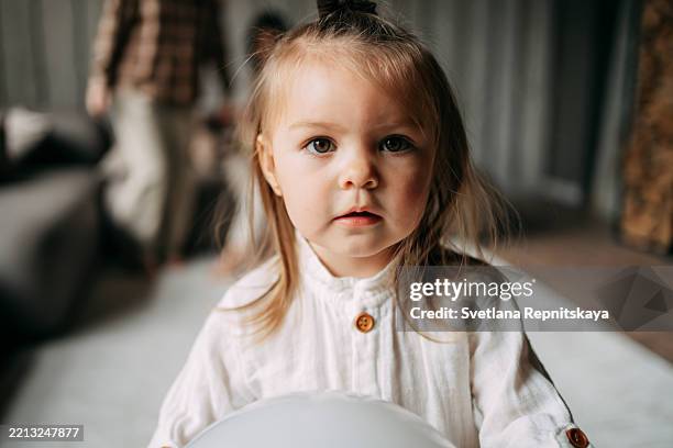 portrait of cute toddler girl holding a white balloon at home - innocenza foto e immagini stock