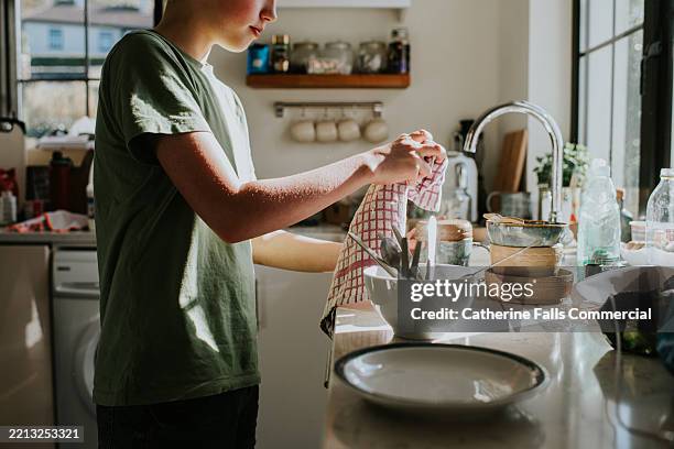 a child dries the dishes while in a cozy, sunlit kitchen during the afternoon hours - attrezzi per le pulizie foto e immagini stock