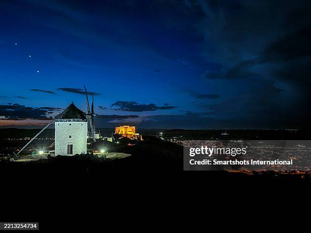 traditional windmills (don quixote's windmills) aligned and illuminated at dusk after sunset under dramatic sky in consuegra with consuegra castle in the background in castilla la mancha, spain - iberian peninsula stock pictures, royalty-free photos & images