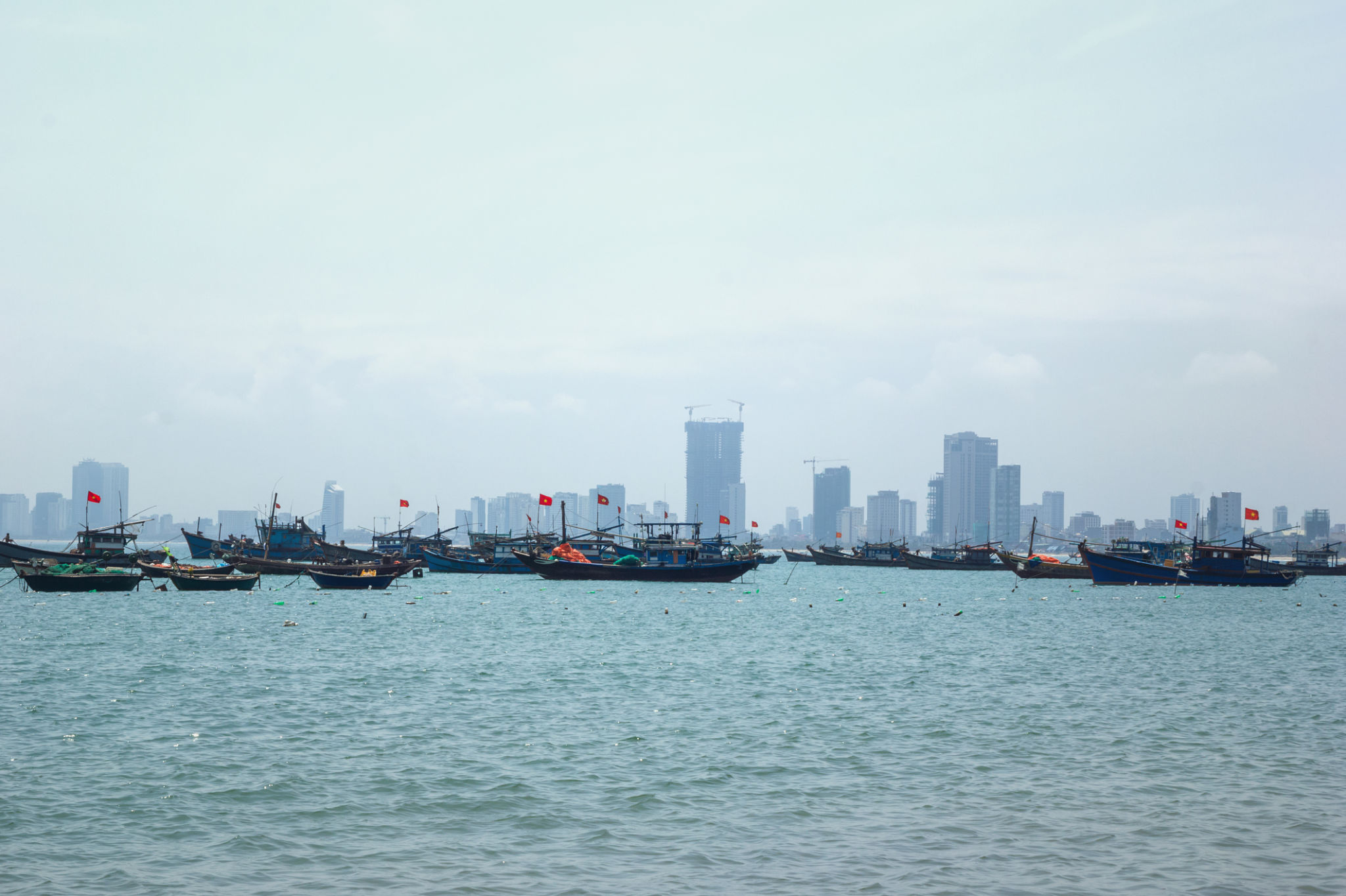 Small fishing boat sailing on calm sea with a large city skyline in the foggy. Danang, Vietnam. Small fishing boat sailing on calm sea with a large city skyline in the foggy. Danang, Vietnam.