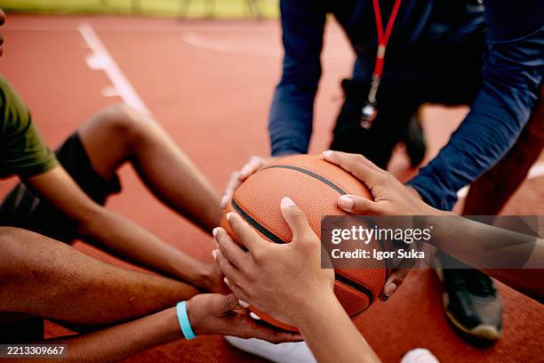 coach and basketball players holding ball together on court - high school basketball stock pictures, royalty-free photos & images