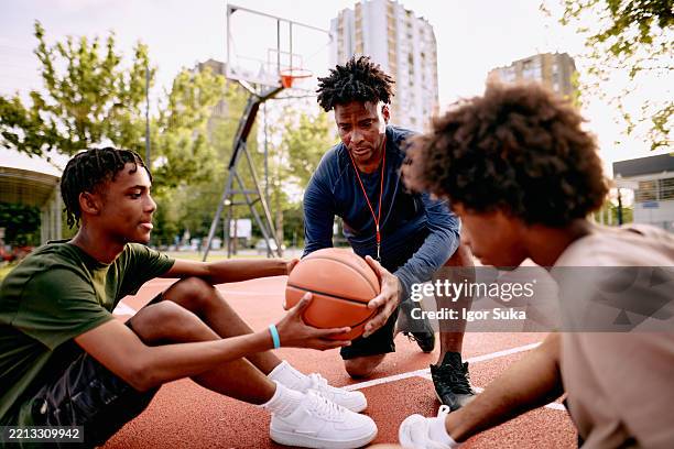 coach mentoring teens on basketball court in outdoor urban setting - basketball coach stock pictures, royalty-free photos & images