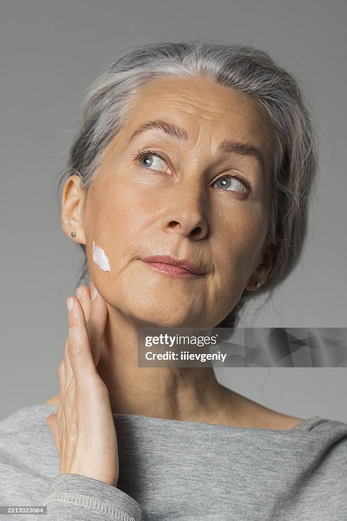 Reife Frau mit Creme im Gesicht. Hautpflege