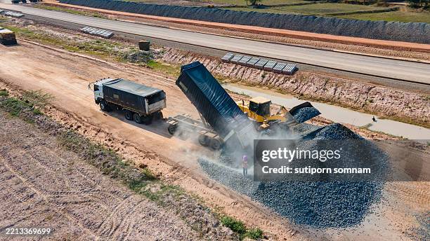 dump truck unloading gravel at road construction site with bulldozer - movimiento de tierras fotografías e imágenes de stock