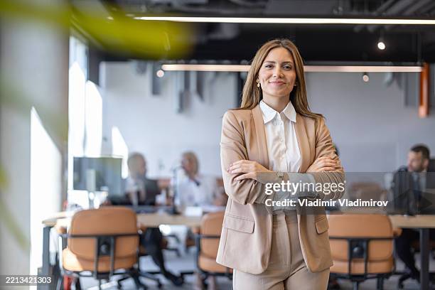 professional woman standing with arms crossed in office - fato imagens e fotografias de stock